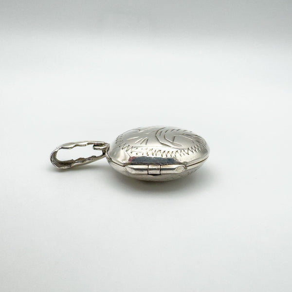 Hinged view of silver locket with engraved foliate bail